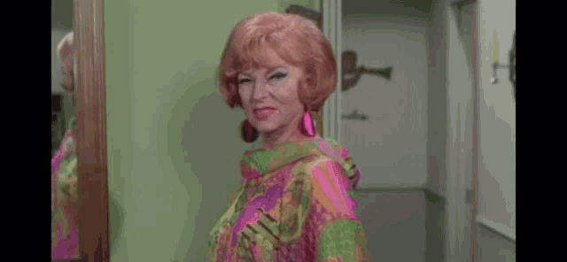 a woman in a colorful dress is standing in front of a mirror and smiling .