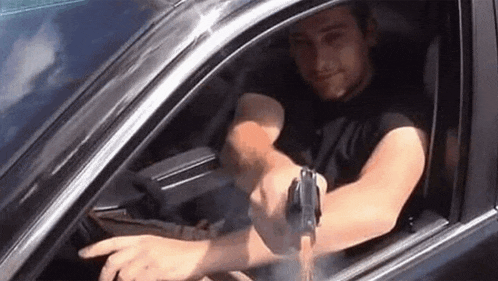 a man is holding a gun while driving a car .