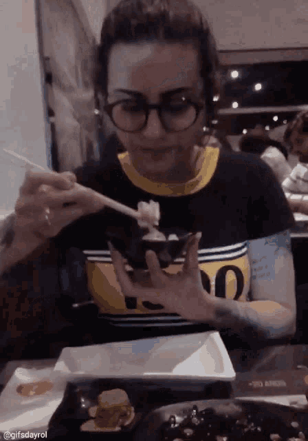 a woman wearing glasses is eating food with chopsticks while wearing a shirt that says 00