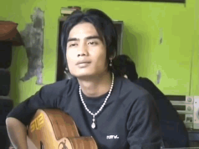 a young man is holding a guitar and wearing a necklace that says ste on it
