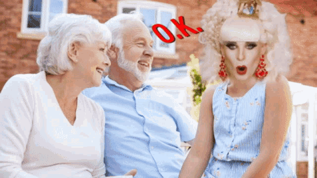 a drag queen is talking to two elderly people and the word ok is visible in red