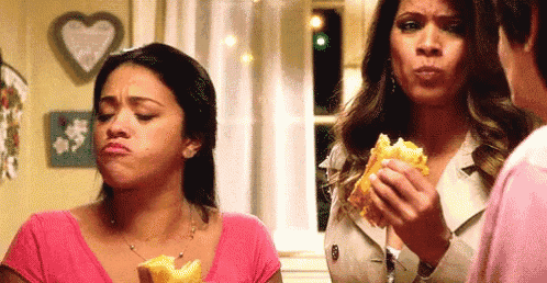 two women are standing next to each other eating food .