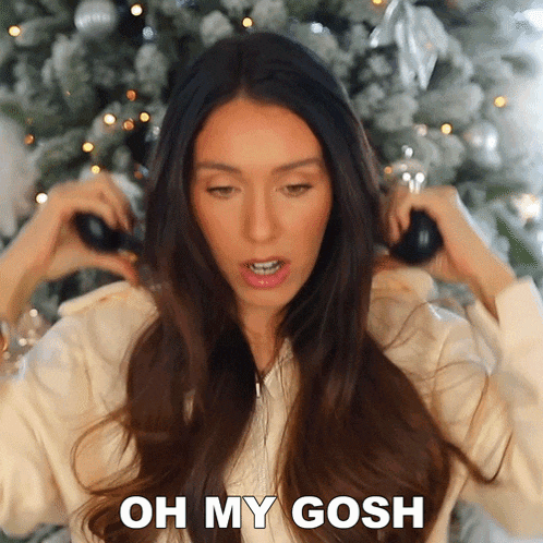 a woman in front of a christmas tree is saying " oh my gosh "