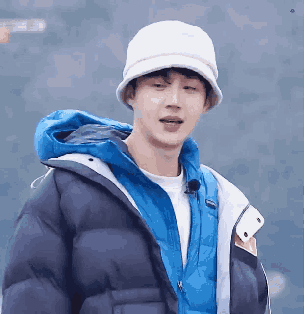 a young man wearing a white hat and a blue jacket is looking at the camera .