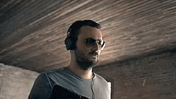 a man wearing headphones and sunglasses is standing in a room .