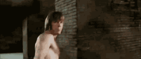 a man without a shirt is standing in front of a brick wall in a dark room .