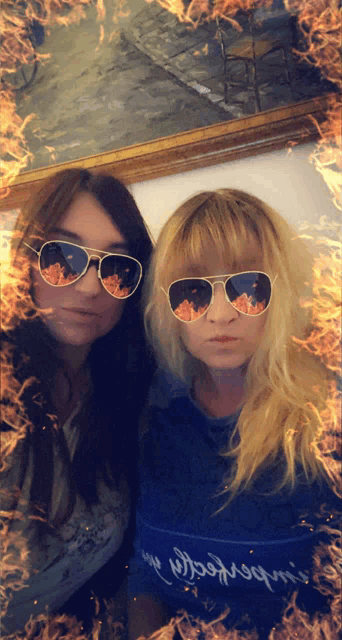 two women wearing sunglasses are standing next to each other with fire behind them