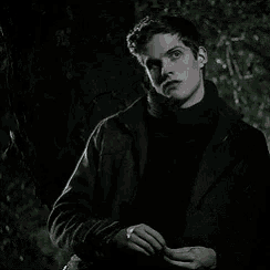 a man in a black jacket and turtleneck is standing in the dark .