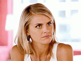 a woman with blonde hair is wearing a white tank top and earrings and making a funny face .