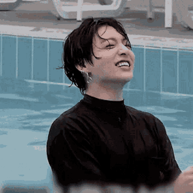 a young man is standing in a swimming pool wearing a wet shirt and earrings .