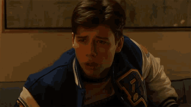 a young man wearing a blue and white varsity jacket with the letter v on the sleeve
