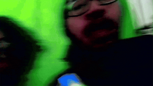 a blurry picture of a man with glasses and a beard in front of a green background