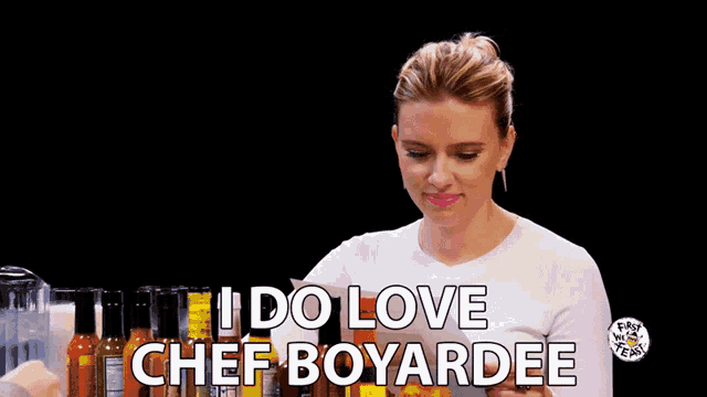 a woman in a white shirt is holding a bottle of hot sauce and says " i do love chef boyardee "