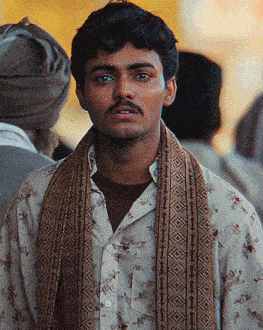 a man with a scarf around his neck looks at the camera with his eyes closed