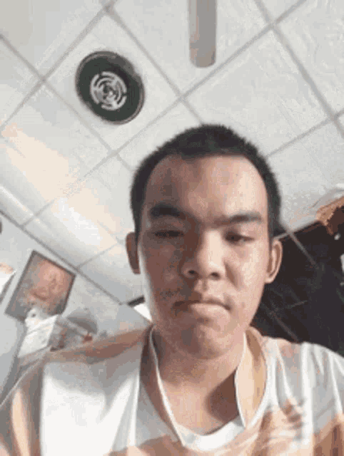 a young man is taking a selfie in a room with a ceiling fan in the background .