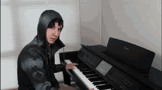 a man in a hooded jacket is playing a piano