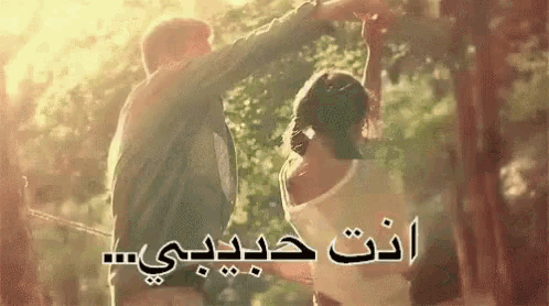a man and a woman are dancing in the woods with arabic writing behind them .