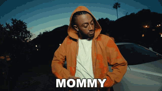 a man in a hoodie is standing in front of a car and says mommy