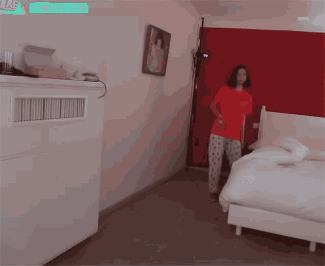 a woman in a red shirt is standing in a bedroom with a red wall