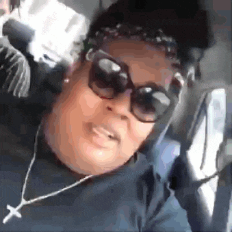 a woman wearing sunglasses and a cross necklace is smiling while sitting in a car .