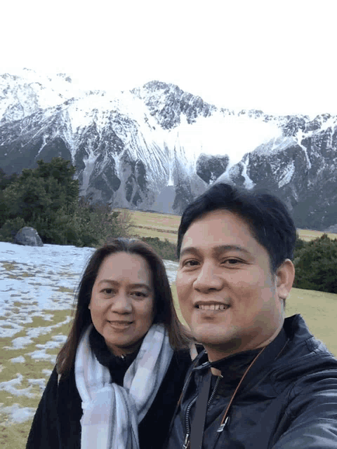 a man and a woman are posing for a picture in front of snowy mountains