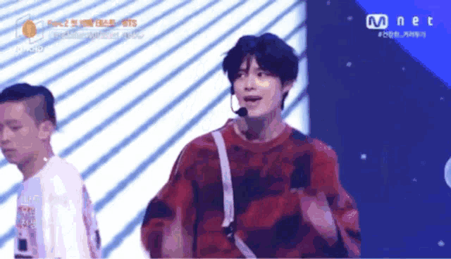 a man in a red sweater is dancing on a stage with a mnet logo in the corner