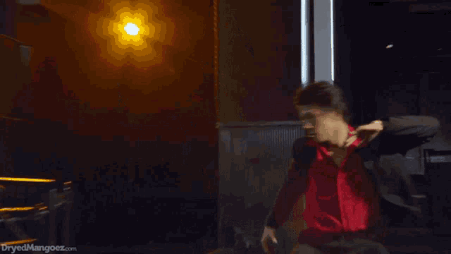 a man in a suit and red shirt is dancing in a dark room with the website dryedmangoez.com in the corner