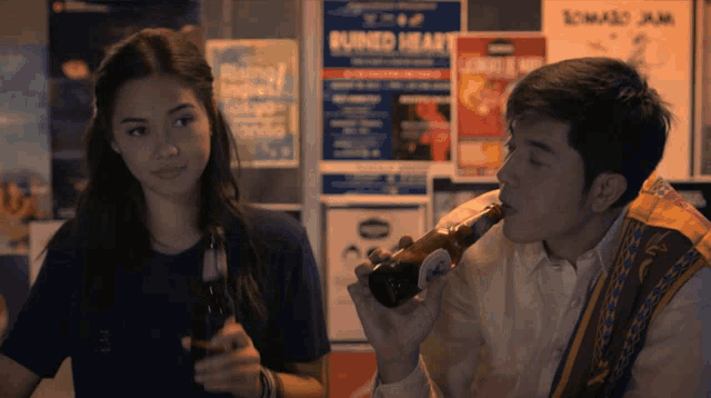 a man drinking from a bottle next to a woman with burned head posters on the wall