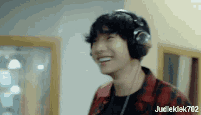a man wearing headphones and a plaid shirt is smiling in a room .