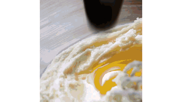 a close up of a bowl of whipped cream with a yellow liquid coming out of it