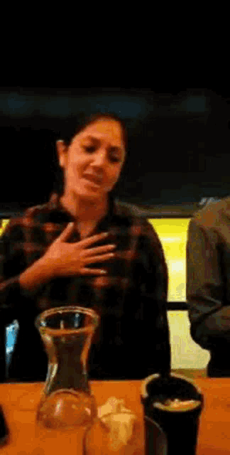 a woman in a plaid shirt is sitting at a table with a glass and a pitcher .