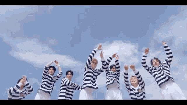 a group of men in striped shirts are standing in front of a blue sky with their arms in the air