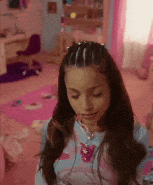 a girl is standing in a pink room wearing a necklace and a braided hairstyle .