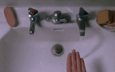 a person 's hand is reaching into a bathroom sink with a red knob on the faucet