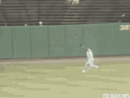 a baseball player is catching a ball on a field with a green fence in the background .
