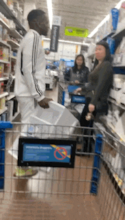 a man is pushing a shopping cart in a grocery store while a woman looks on .
