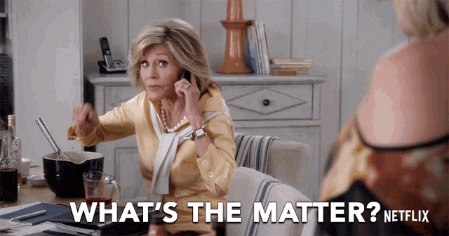 a woman sitting at a table talking on a cell phone with the words what 's the matter netflix behind her