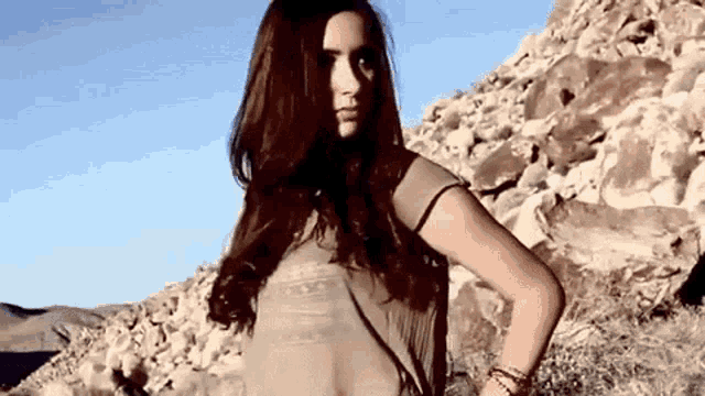 a woman in a sheer top is standing in the desert .