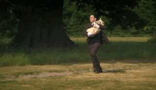 a man in a suit is running with a dog in his arms in a field .