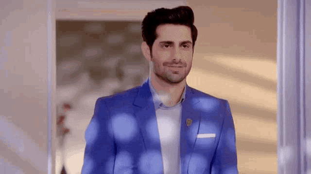 a man in a blue suit and white shirt is standing in a room .