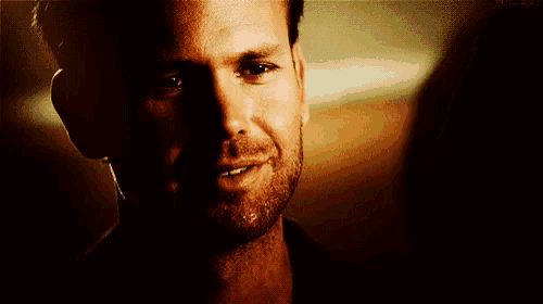 a man with a beard is smiling and looking at the camera in a dark room .