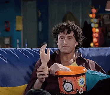 a man is sitting on a couch holding a glove and a bucket