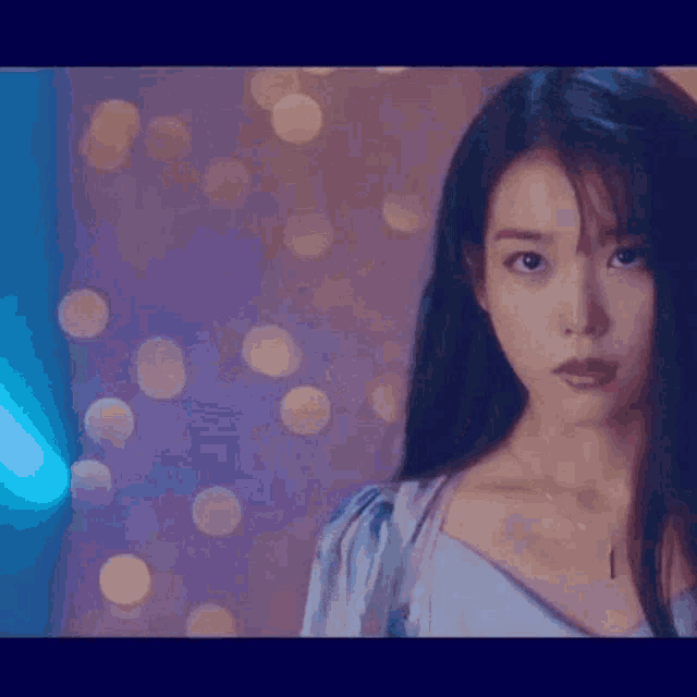 a woman in a blue dress is standing in front of a wall with lights .