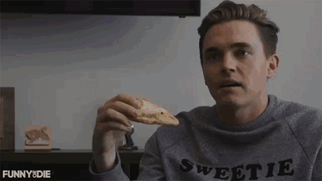 a man in a sweetie shirt is eating a cookie .