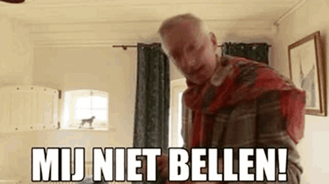 a man is standing in a living room with a red scarf around his neck and the words `` mij niet bellen ! ''