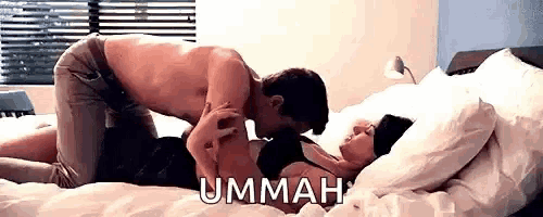 a man and a woman are kissing on a bed and the man is kneeling on the woman .