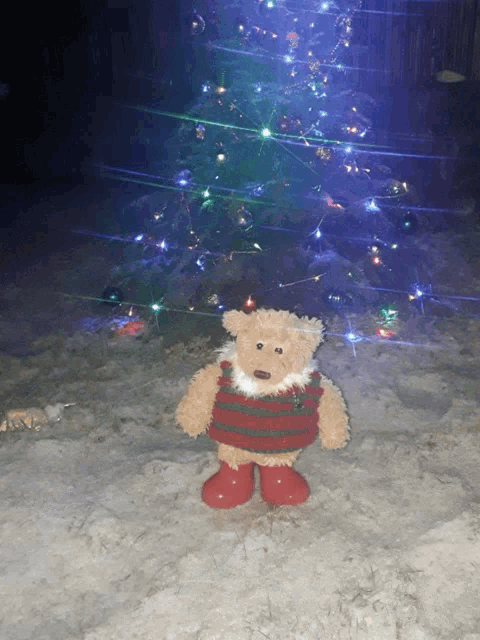 a teddy bear standing in front of a christmas tree with lights