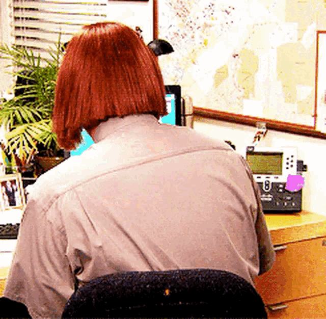 a woman with red hair is sitting at a desk with a phone and a computer