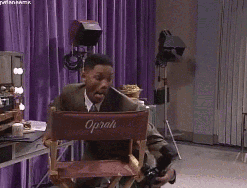 a man is sitting in a director 's chair with a purple sign that says oprah