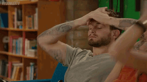 a man with a tattoo on his arm is sitting on a couch with his hand in his hair .
